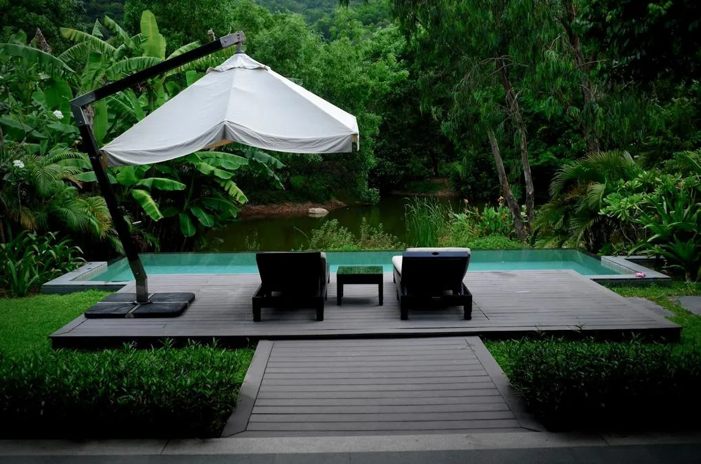 A wood deck next to a small pool with two lounge chairs and an umbrella
