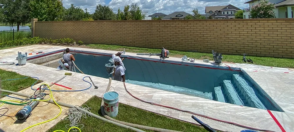 Workers from a pool finishing company spraying plaster finish on the interior of a swimming pool