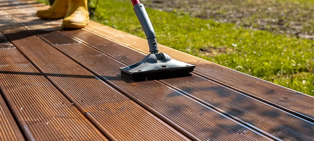 applying stain to wooden deck with a brush on sunny day
