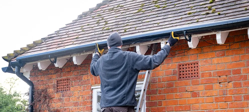 man on a ladder fixing fitting a gutter on the eaves of a house