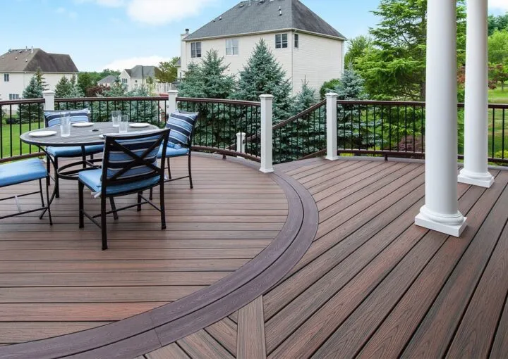 Curved composite deck with dining set and elegant railing, offering scenic suburban views.