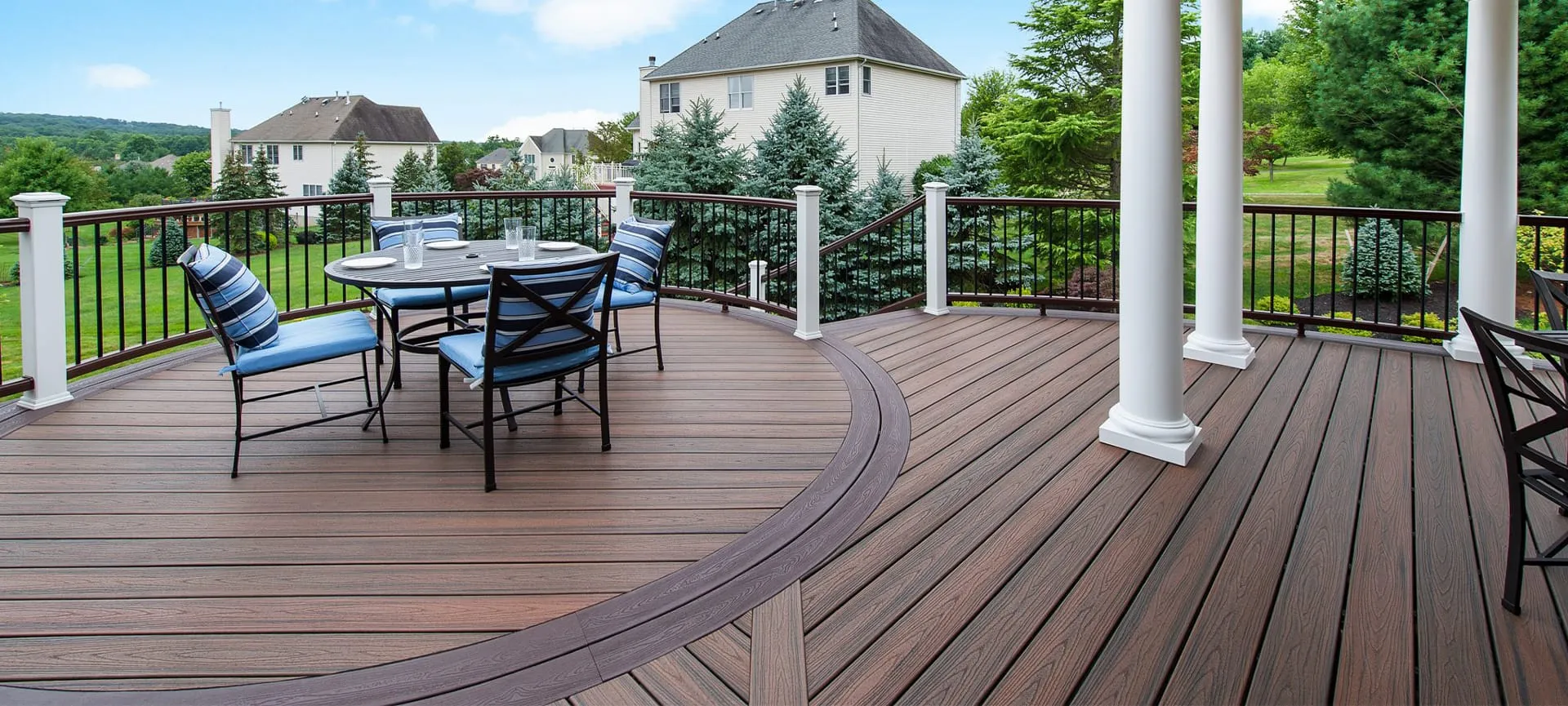 Curved composite deck with dining set and elegant railing, offering scenic suburban views.