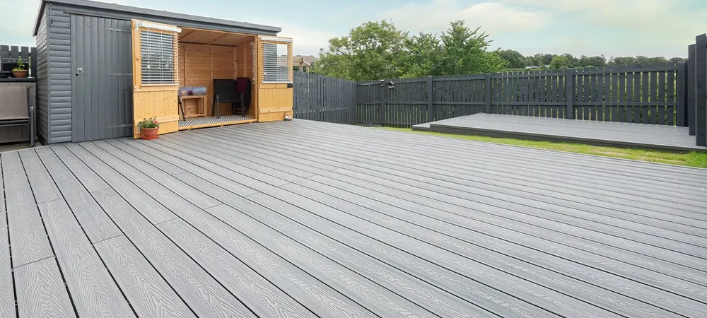 Large grey composite deck with wooden shed and black fence in a sunny backyard setting