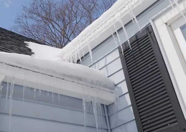 snow-covered roof with icicles showing winter damage risks to home gutter systems