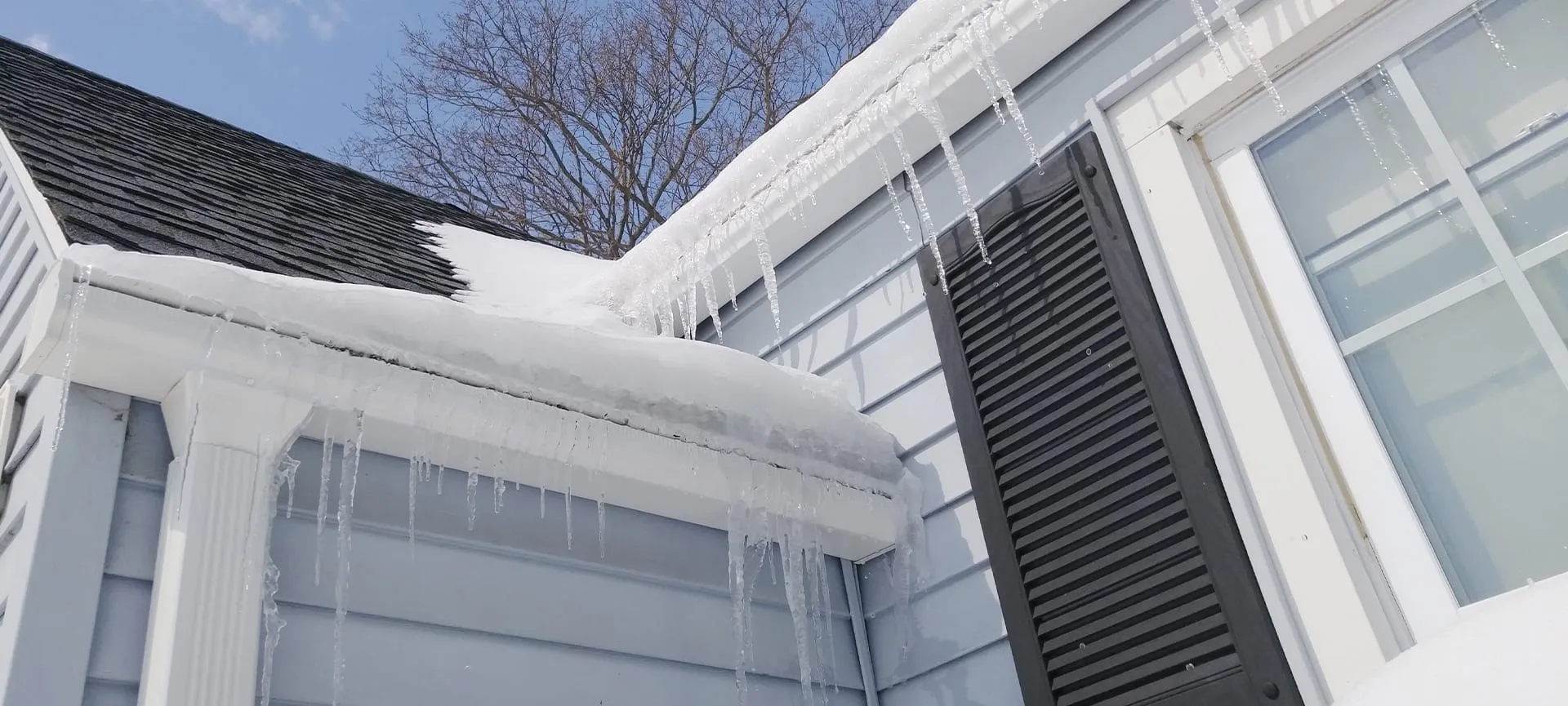 snow-covered roof with icicles showing winter damage risks to home gutter systems