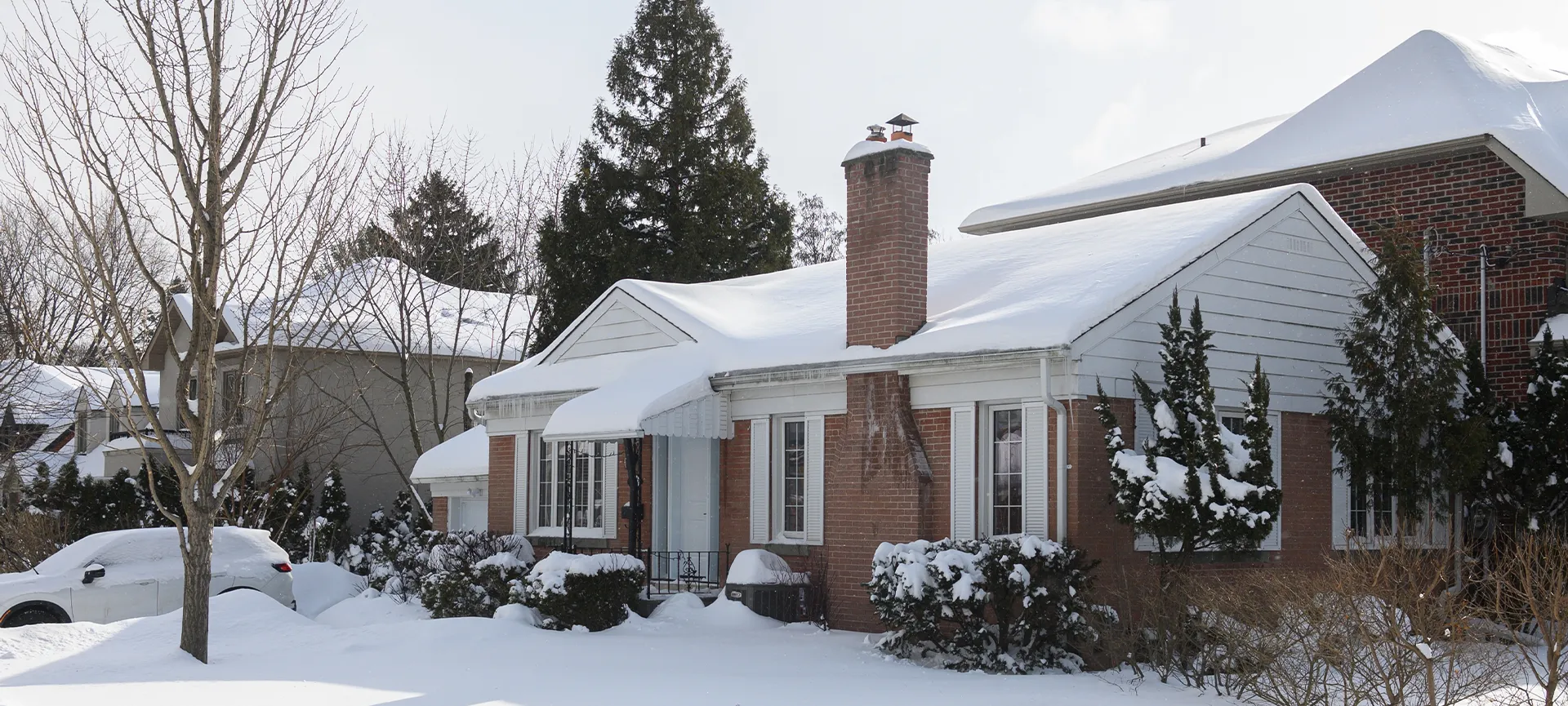 suburban house stands covered in snow with icicles hanging from the roof, while the sunlight casts shadows on the white winter landscape