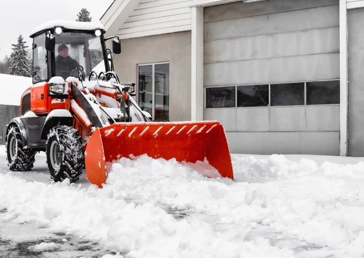 Little red tractor with snowplow in a motion removing snow
