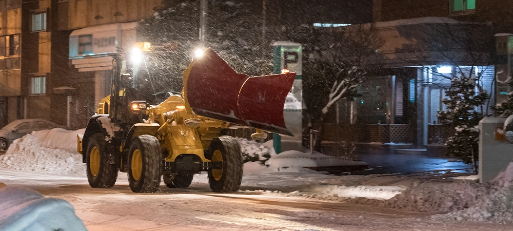 Winter weather, snow on the road, falling tree. Snow calamity on the road. Snow removal vehicle at work at night