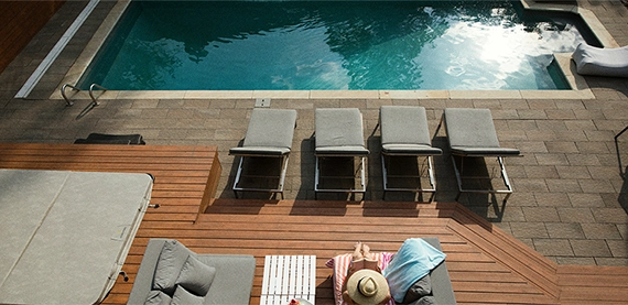 women sitting on chair in wooden deck look at pool. concrete pool with interlocking surface