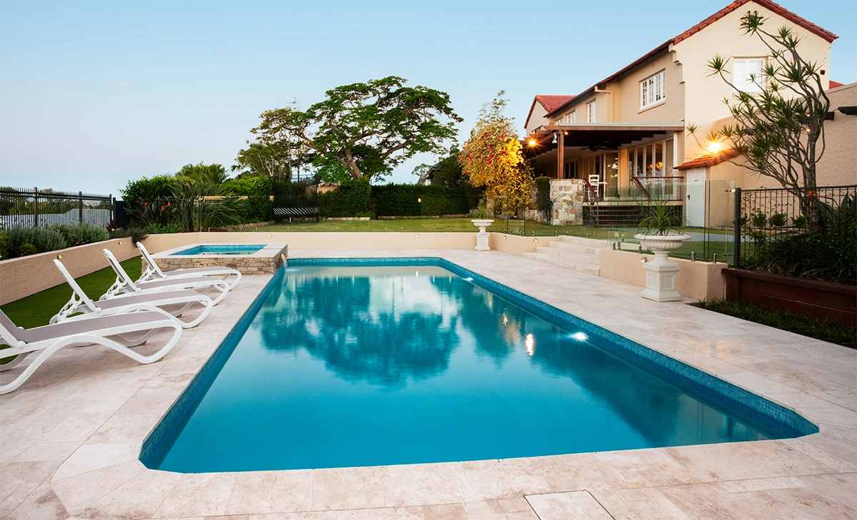 concrete pool with waterfall feature and luxury interlocking floor in side of home backyard