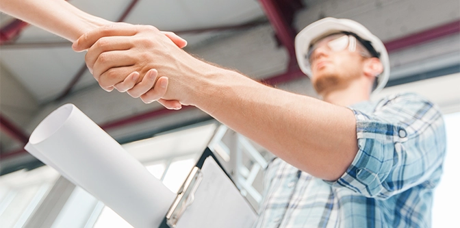 architecture and home renovation concept - builder with blueprint shaking partner hand