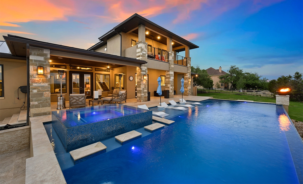 home backyard full view, luxury infinite concept concrete pool with walkway step, lighting on and firepit in lawn