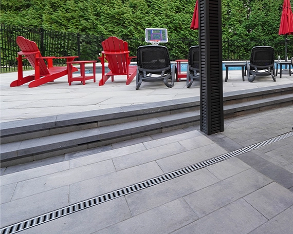 backyard interlock patio with steps , chairs around pool, water drainage system