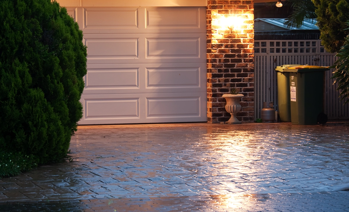 close view of permeable driveway, white garage door and lighting on, night view, after rain, wet driveway