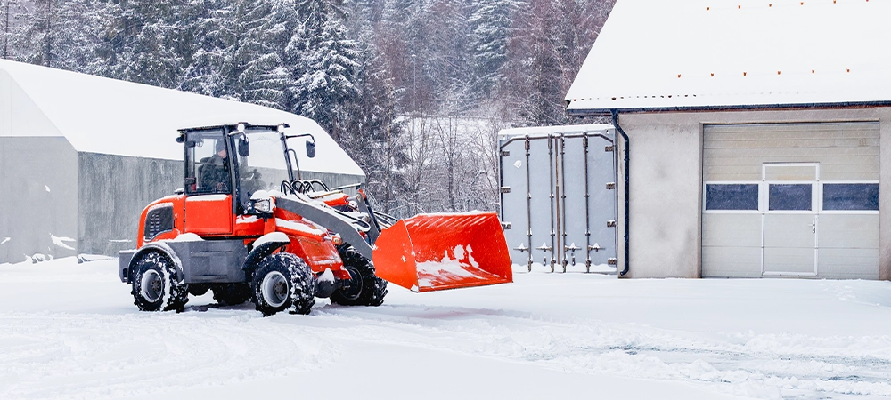 Red tracor cleaning snow in snowstorm. Blizzard weather conditions. Winter time street maintenance.