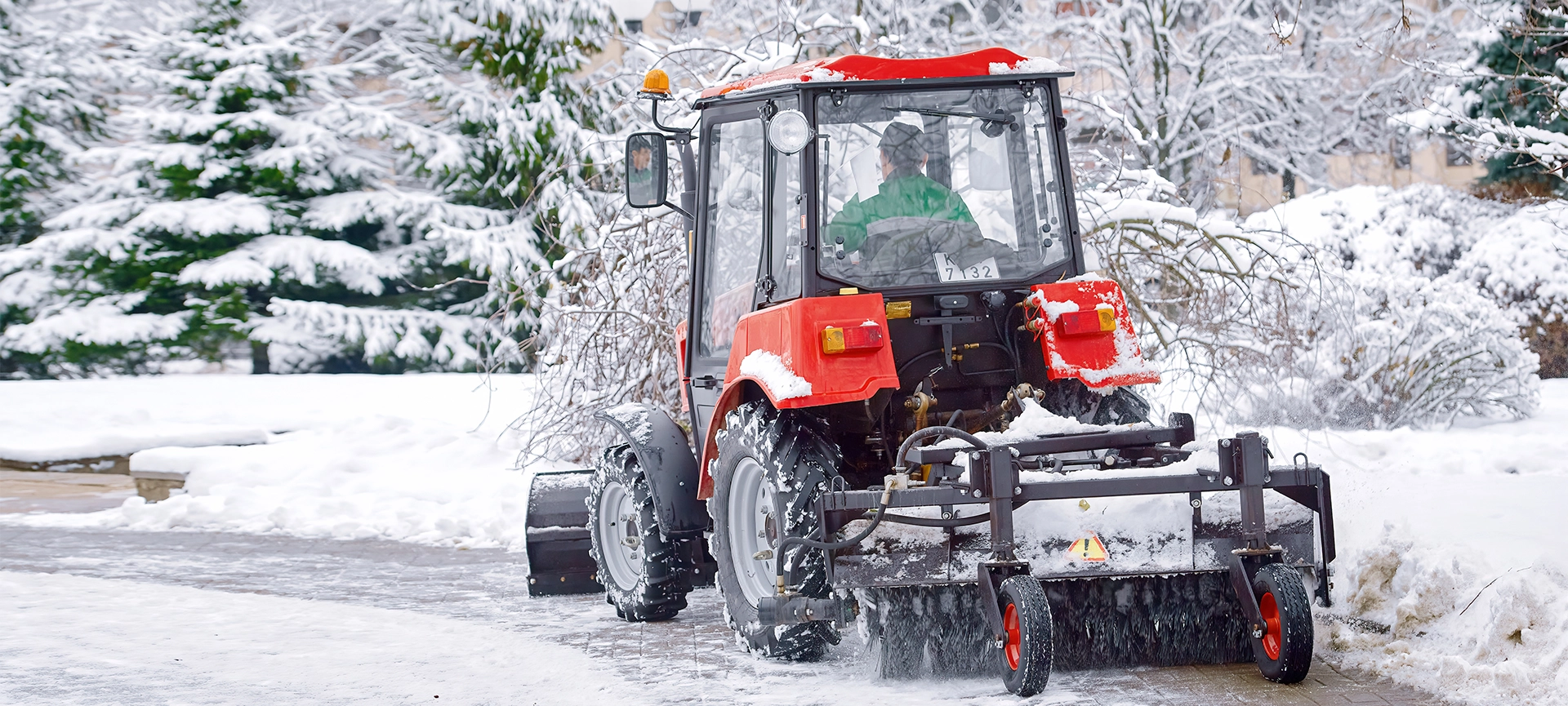 Tractor clear snow in park, machinery cleaning equipment. Snow removal red tractor clean walkway with plough sweeping brush. Tractor removing snow, cleaning sidewalk from snow in snowy winter