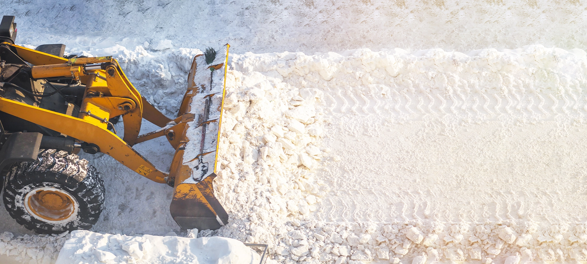 A large orange tractor removes snow from the road and clears the sidewalk. Cleaning and clearing roads in the city from snow in winter. Snow removal after snowfalls and blizzards.