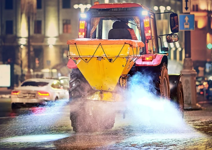 Tractor with salt spreader plow snow, spread salt on pavement after snow storm, road maintenance - winter gritter vehicle. Tractor de-icing street, spreading salt. Machinery spreader salting sidewalk