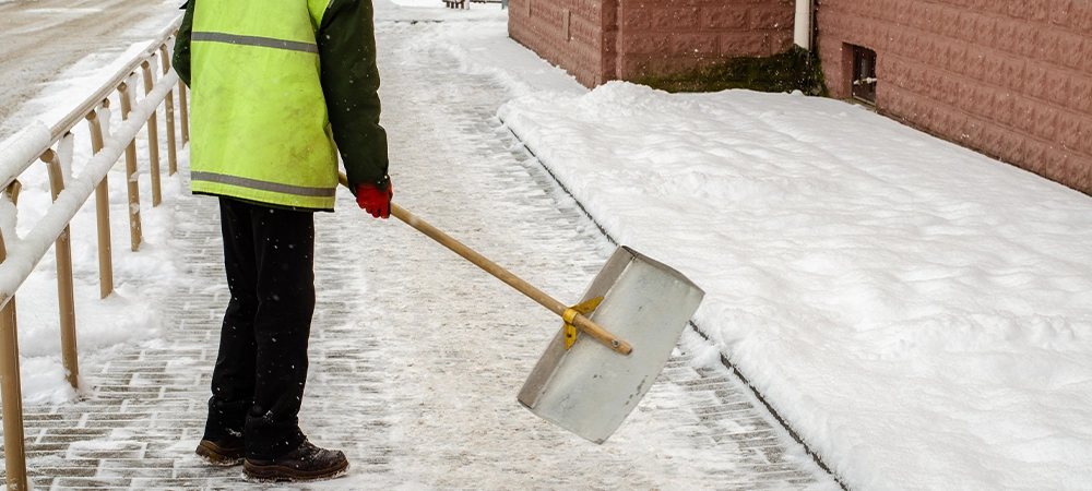 snow storm in the city. Roads and sidewalks covered with snow. Worker shovel clears snow. Bad winter weather. Street cleaning after snowstorm.