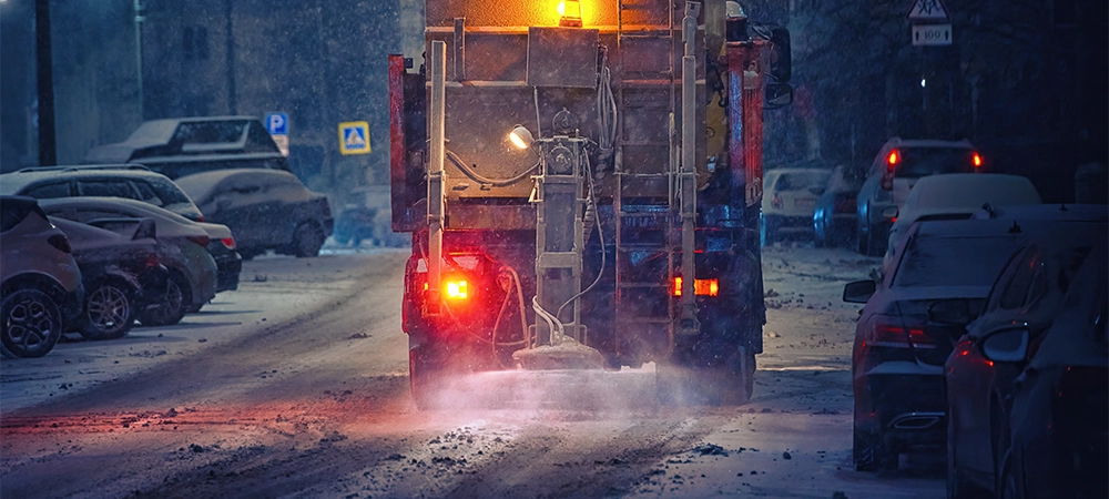 Salt spreading. Snow plow service truck removing snow and spreading salt on snowy city road during blizzard, night work road maintenance. Truck spreading de-icing salt on snowy and icy asphalt road