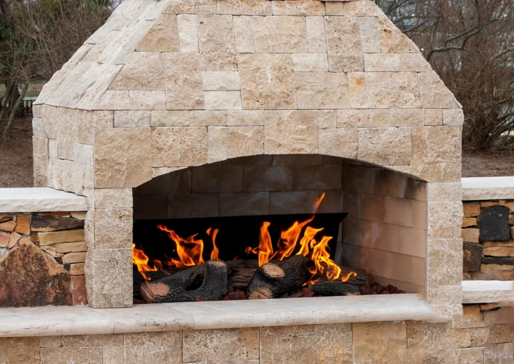A gas fireplace made from paving stone burning outside on a patio close up.