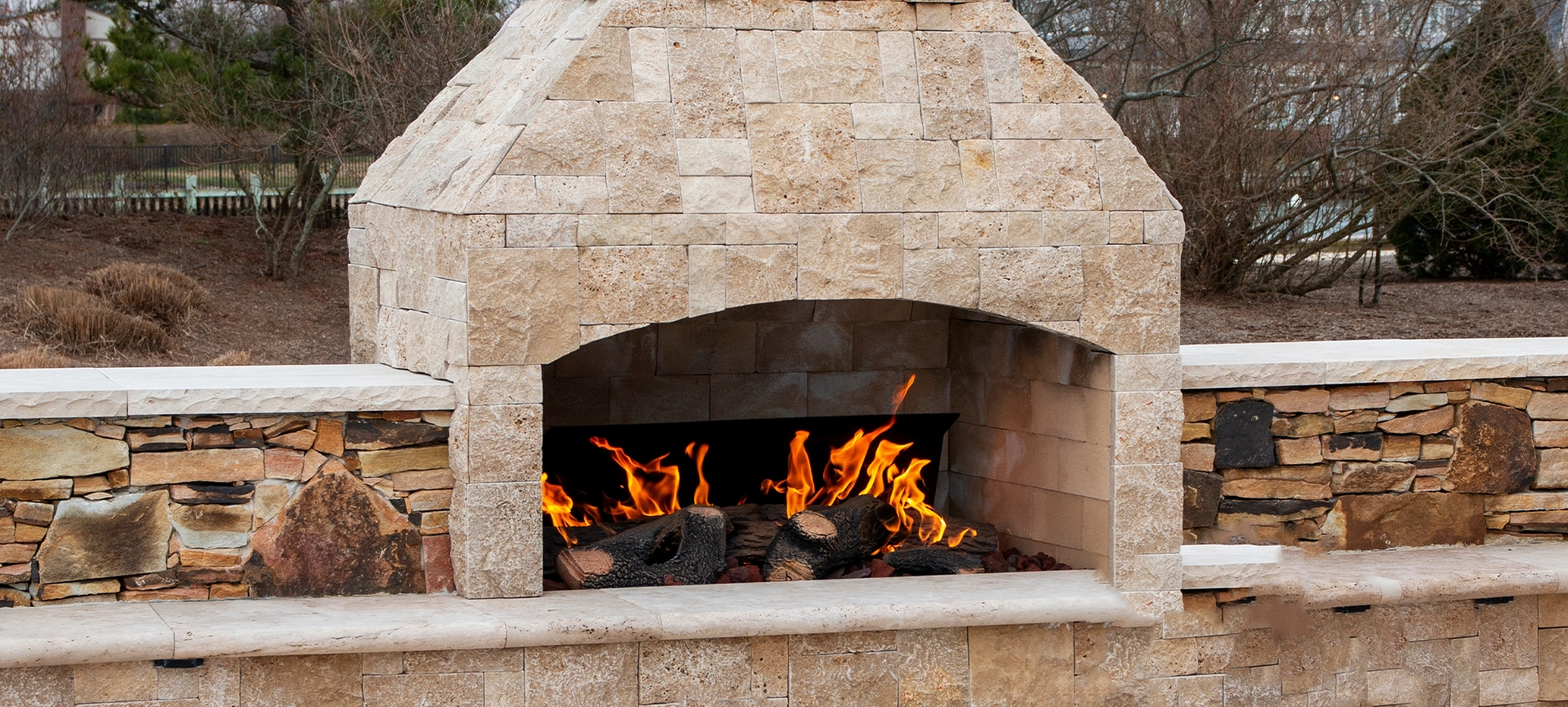 A gas fireplace made from paving stone burning outside on a patio close up.