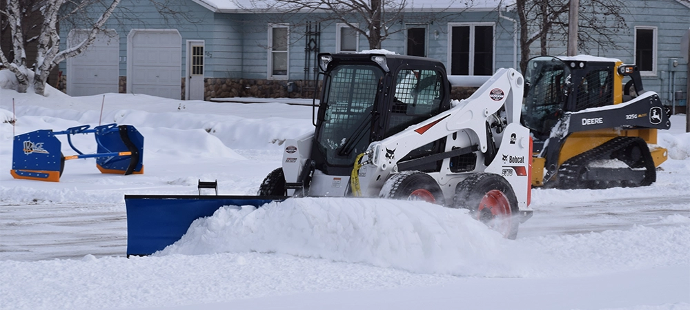 Bobcat skid steer with snow tires and KAGE snow pusher clearing snow from a parking lot