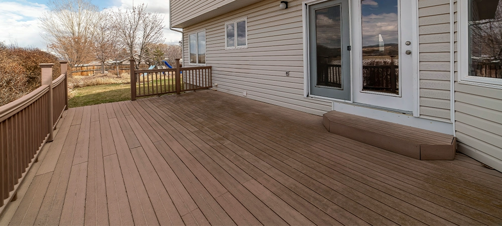 Spacious wooden deck of house overlooking the grassy backyard with playground