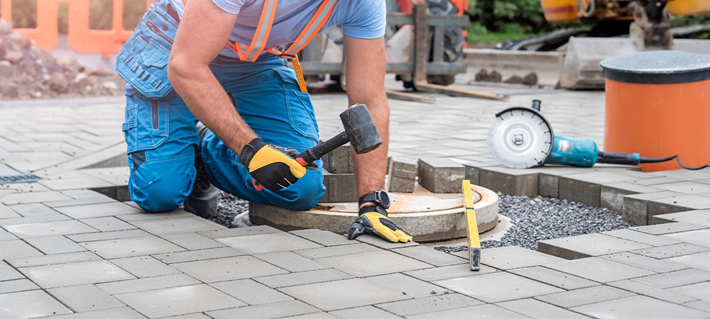 Laying interlocking paving. A worker is placing interlocking paving stones around the sewer manhole cover.