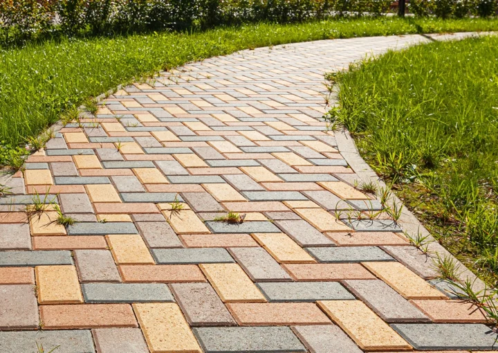 The pedestrian path is paved with multi-colored paving stones. Grass grows between the tiles. Selective focusing.