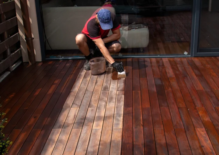 Exterior hardwood deck annual refreshing, man with paintbrush applying nourishing oil on cleaned and sanded Ipe decking terrace boards