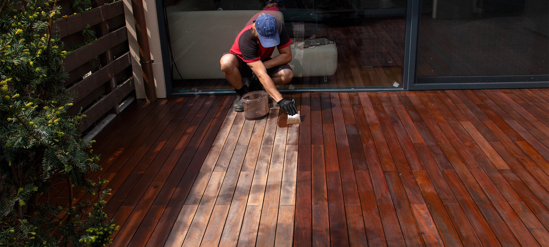 Exterior hardwood deck annual refreshing, man with paintbrush applying nourishing oil on cleaned and sanded Ipe decking terrace boards