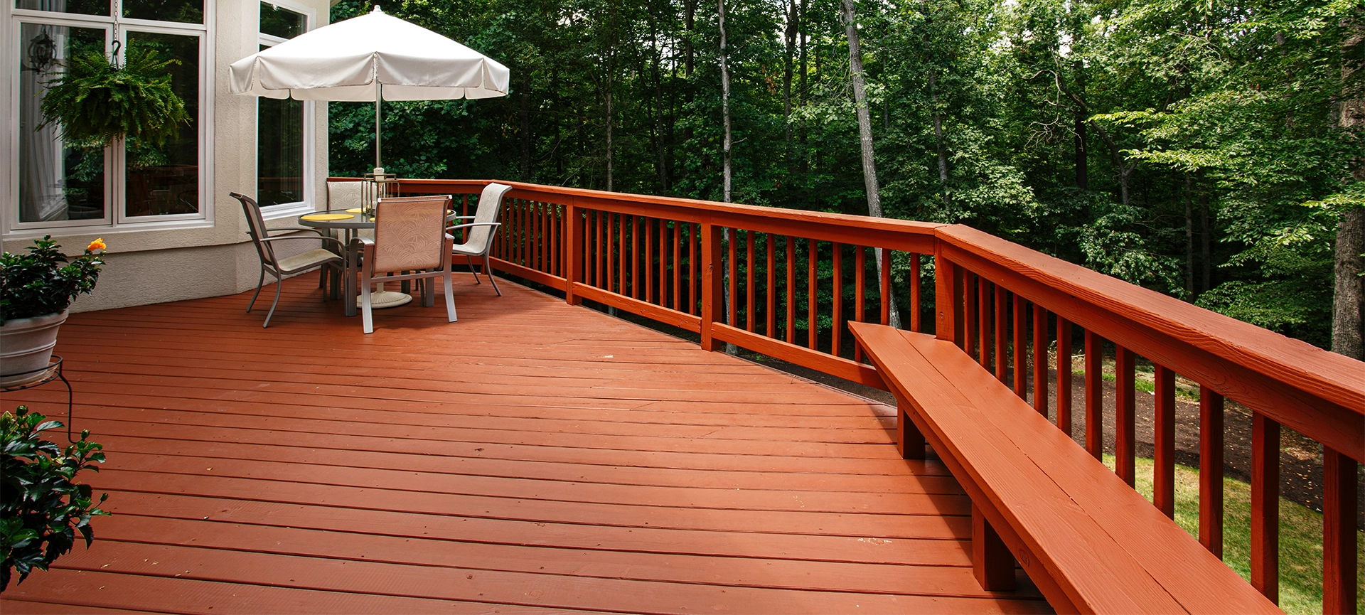 Large Wooden Deck Featuring an Umbrella-Covered Outdoor Dining Set Surrounded by A Dense Forest in Summer