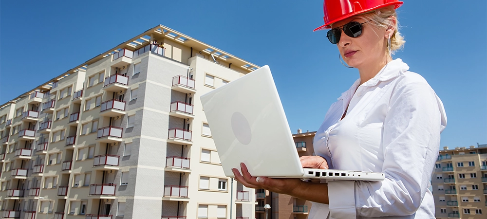 condo maintenance partner, contractor woman holding laptop in hand and standing nearby condo buildings