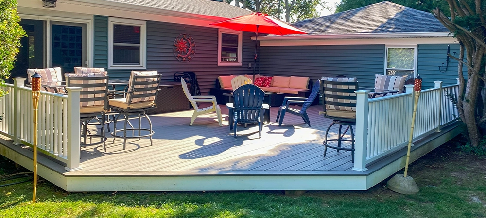 A deck set up with a table and chairs shaded by a large umbrella. The furniture is arranged neatly, creating a cozy outdoor dining area.