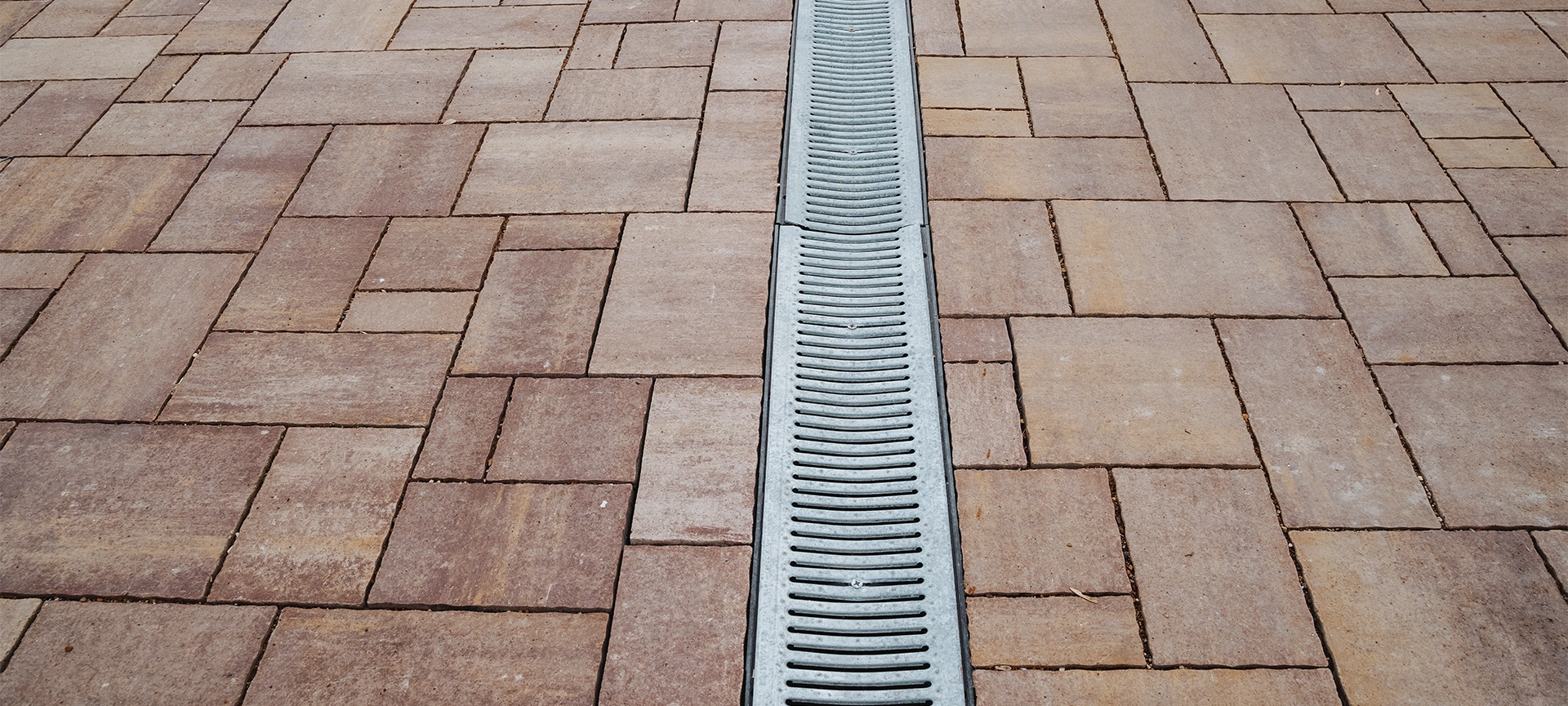 This image shows a closeup of a brick driveway drain, highlighting the intricate brick textures and the cleverly integrated drainage system that enhances both functionality and aesthetics