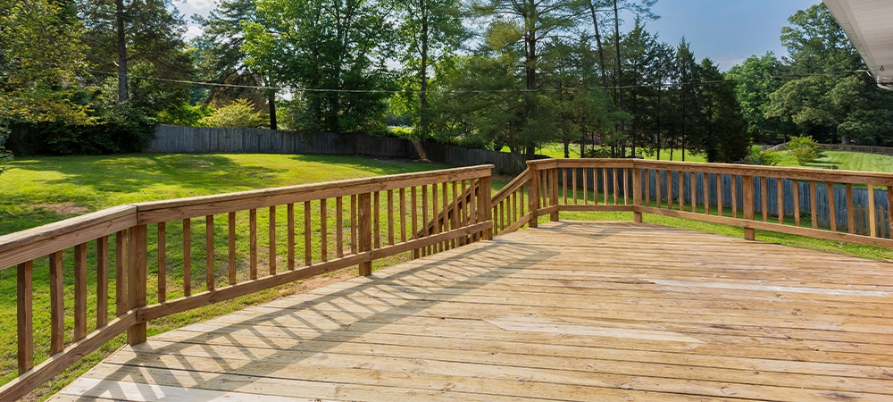 Spacious Wooden Backyard Deck With Green Lawn And Trees Under Clear Sky