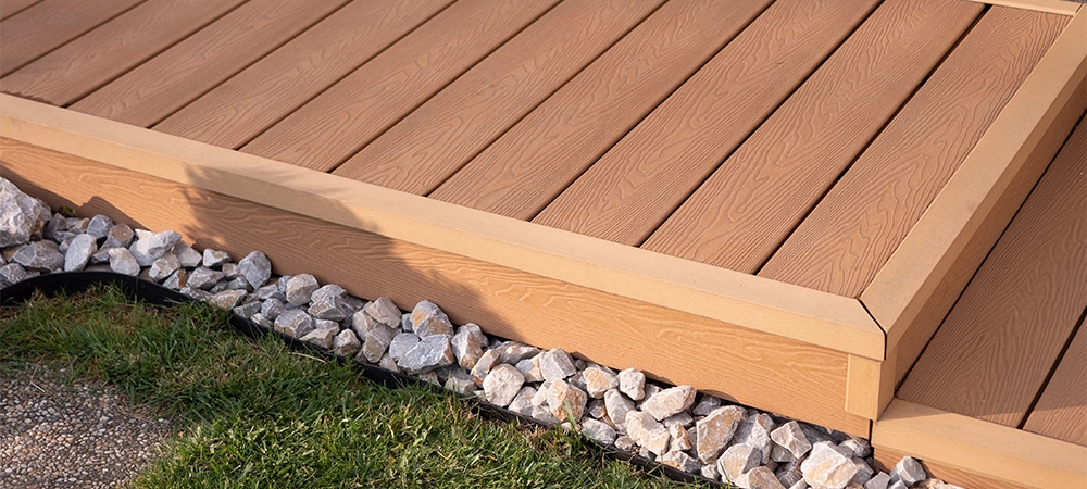 Composite WPC terrace decking with step and corner trim, garden walkway detail with grass and decorative stones, close-up.
