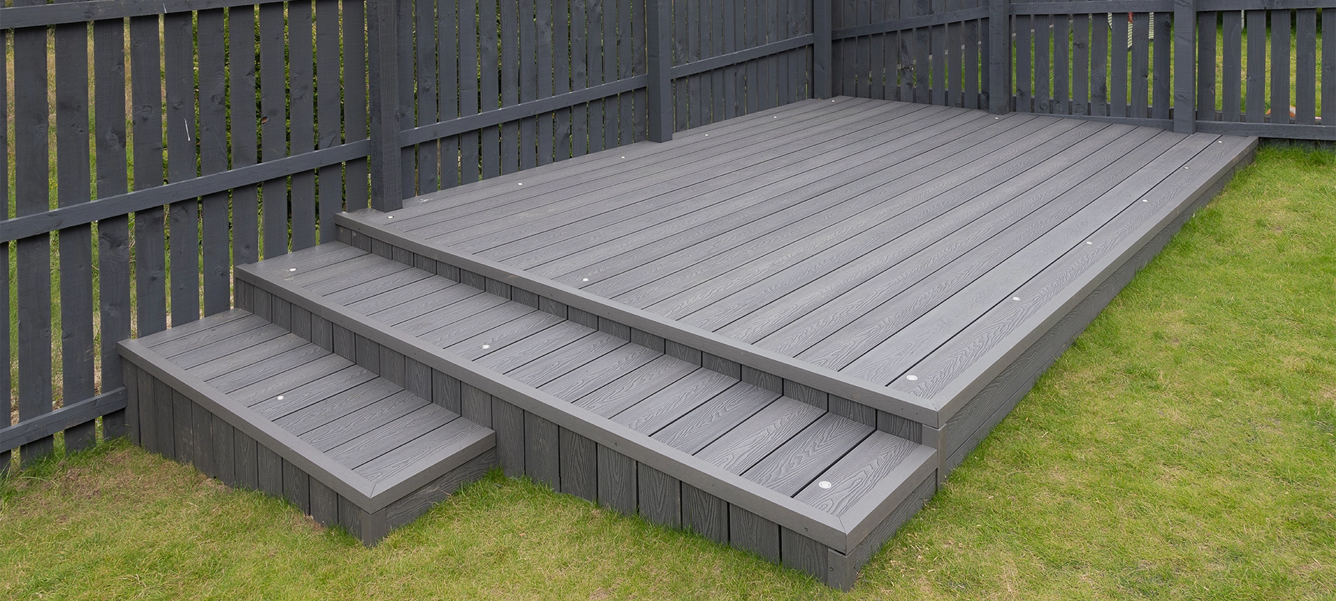 Ash grey composite decking built on two levels on a residential back garden with low voltage deck lights installed as well. Good Image for a landscape Gardiner